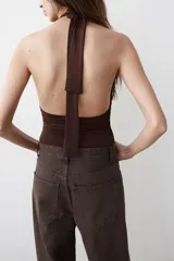 Body de cuello halter confeccionado en mezcla de poliamida, con abertura frontal y aplicación metálica forrada. Presenta diseño drapeado en los laterales, espalda descubierta y cierre inferior con botones a presión.
