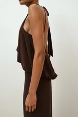Vestido largo de color marrón oscuro con cuello halter y lazada en la nuca. Presenta un diseño con detalle de tejido drapeado efecto globo en la cintura y corte recto en la falda.