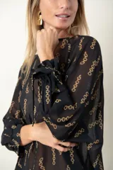 Blusa negra de gasa con estampado de cadenas doradas, escote redondo y mangas largas abullonadas con lazos en los puños.