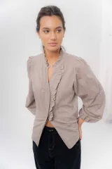 Camisa de manga larga color beige con diseño a rayas sutiles, cuello mao con volados y abertura frontal con detalles de volados a un lado.