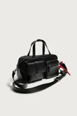 Bolso bandolera negro de acabado liso, con compartimento principal con cierre de cremallera. Cuenta con dos bolsillos frontales, uno con solapa y detalle metálico y otro con cremallera. Incluye dos asas de mano y un asa de hombro ajustable y extraíble, además de detalles de charms y mosquetón en un lateral.