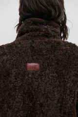 Chaqueta tipo gamulán de color marrón, con solapas amplias forradas en corderito sintético oscuro. Presenta un diseño cruzado con botones frontales y mangas largas, ideal para un estilo invernal.