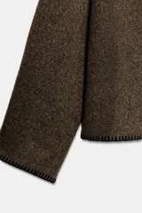 Jersey de punto color marrón con cuello barco y manga larga. Presenta pespuntes decorativos en color negro a contraste en el cuello, puños y bajo.