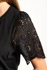Remera de algodón peinado color negro, con mangas cortas de broderie con diseño calado y terminación festoneada. Presenta un corte oversize y cuello redondo.