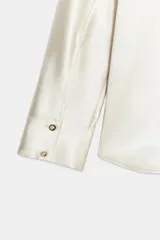 Camisa de manga larga confeccionada en tejido satinado, con cuello solapa, cierre frontal con botones y bajo asimétrico.