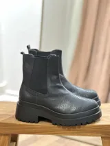 Bota estilo Chelsea de cuero con textura, color marrón oscuro, con paneles elásticos laterales negros y suela de plataforma dentada de goma negra.