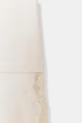 Remera color crema de algodón, corte recto, cuello redondo y mangas cortas. Presenta un panel asimétrico de encaje en el ruedo.