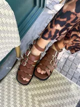 Sandalias planas de cuero color marrón, con tiras anchas y hebillas plateadas.