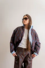 Pantalón sastrero de tiro medio con cierre frontal visto y bolsillos laterales. Presenta un diseño de corte recto y amplio con estampado floral sutil sobre fondo marrón.