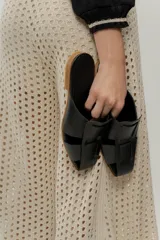 Zueco de cuero color marrón, estilo mule, con puntera cuadrada y tira ancha adornada con flecos. Suela plana.