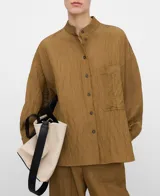 Camisa de efecto arrugado color tostado, con cuello mao, cierre frontal de botones, manga larga y bolsillo de plastrón en el pecho.