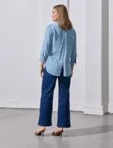 Camisa gris de tencel con cuello con solapa, escote en V y abertura central con botones. Largo de manga regulable con presilla y botón. Ruedo en espalda con tajo.