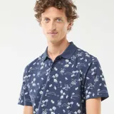 Remera polo azul marino con estampado de palmeras, barcos y paisajes playeros en blanco. De corte clásico y manga corta.