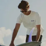 Remera de manga corta color blanco, con cuello redondo y logo de la marca Rhythm estampado en el pecho en un recuadro azul.