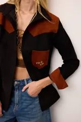 Sobrecamisa de gamuza color marrón con apliques de cuero metalizado en tono cobre en los hombros y bolsillo frontal. Presenta detalles bordados en las mangas, el bolsillo y la espalda, con un diseño de corte recto y cuello camisero.