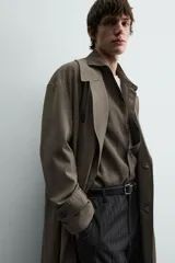 Trench color verde militar, de corte oversized, con cuello con solapas de muesca y manga larga con puño y trabilla. Presenta bolsillos de plastrón con solapa en la cadera y un bolsillo interior. Tiene una abertura en el centro de la espalda y cierre frontal de botonadura cruzada.