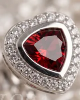 Aros tipo caravana de plata con diseño triangular y piedra central de circonia en forma de corazón color granate, rodeada por pequeñas circonias blancas.