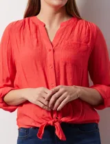 Blusa blanca de gasa marca Zac & Rachel, con cuello a la base, escote en V, abertura central con botones, bolsillo aplicado en el pecho y mangas largas regulables con presilla y botón. Tiene terminación opcional de nudo en el ruedo.