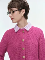 Cárdigan de tejido de punto grueso en color fucsia, con cuello redondo, cierre frontal de botones dorados y puños acanalados.