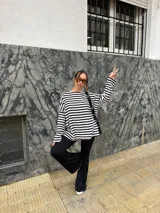 Conjunto compuesto por remera de manga larga oversize a rayas horizontales blancas y negras con escote bote, y pantalón negro de corte flared.
