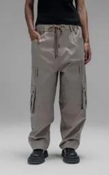 Pantalón cargo de corte oversize y silueta estructurada, confeccionado en microfibra pesada con leve elasticidad. Presenta cintura elástica con cordón de ajuste externo, cierre frontal con botón metálico, bolsillos laterales y bolsillos cargo de gran tamaño con tapa y broches a presión.