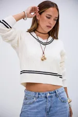 Sweater de punto trenzado color blanco, con cuello en V y detalles de rayas negras en el cuello, puños y ruedo. De corte corto y manga larga.