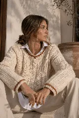 Sweater de lana merino en color crudo, con diseño de tejido trenzado y detalles de terminaciones en contraste color marrón en cuello, puños y cintura. Presenta un corte clásico y tejido de punto grueso.