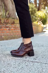 Botines de cuero color marrón oscuro con puntera fina y caña baja. El talón es de cuero con textura de reptil y el taco es geométrico.