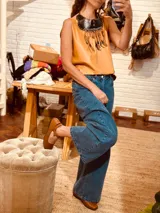 Collar babero de cuero color camel con flecos y detalles de cuentas de madera. Tiene un cuello negro con costuras cruzadas.