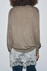 Jersey de punto fino en color marrón topo con escote en pico y manga larga. Presenta un diseño de doble capa con un bajo de encaje floral en color crudo que sobresale en la parte inferior.