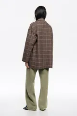Abrigo de corte sastrero con diseño a cuadros en tonos marrones y grises. Presenta silueta estructurada, cuello con solapas, cierre frontal con botones y bolsillos laterales. Las solapas y los bordes cuentan con un acabado desflecado que le otorga un estilo contemporáneo.
