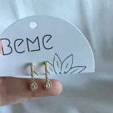 Aros colgantes dorados con forma de lágrima y pequeños brillantes.
