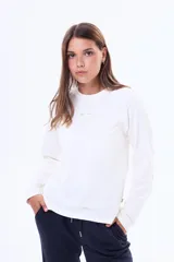 Remera de manga larga en color blanco, con cuello redondo y corte clásico. Presenta una pequeña etiqueta decorativa en el centro del pecho.