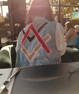 Chaleco de jean celeste con apliques geométricos en terciopelo rojo y negro, bordados a mano.