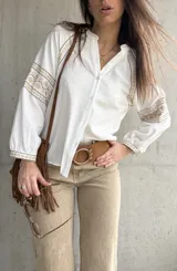 Camisa blanca de calce relajado y tejido liviano, con escote en V y delicados detalles bordados geométricos en tonos tostados en las mangas abullonadas y puños.