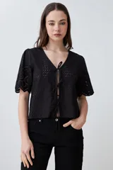 Blusa negra de broderie con escote en V y lazos para atar en el frente. Tiene mangas cortas con terminación de puntilla. 
