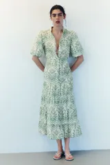 Vestido largo de algodón color blanco con estampado botánico en tonos verdes. Presenta cuello mao, cierre frontal con botones ocultos, mangas cortas abullonadas y falda de corte escalonado con volados. Incluye un cinturón fino para ajustar en la cintura.