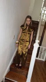 Vestido largo verde de tafeta con silueta entallada, cuello alto, mangas cortas, abertura tipo gota en el escote y hilera de botones frontal.