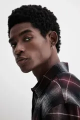 Camisa de franela de manga larga con cuello inglés, tapeta lisa, canesú en la espalda, bolsillo superior abierto y bajo redondeado. Presenta un patrón de cuadros en tonos negro, gris y granate.