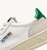 Championes de estilo vintage inspirados en los años 80, confeccionados en cuero blanco con paneles de gamuza gris en la puntera y el talón. Presentan perforaciones en la puntera para mayor ventilación, cordones planos de algodón y un detalle en color verde en el talón. La suela es de goma en tono crema con el logo de la marca.