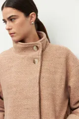 Tapado corto color beige de tejido grueso con cuello alto, cierre frontal con botones grandes veteados y bolsillos delanteros.