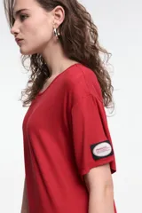 Vestido midi color beige, de corte oversized, con cuello redondo, manga corta y tajos laterales. Presenta un parche decorativo en la manga.