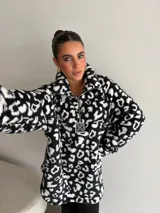 Buzo de peluche con estampado animal print, cuello alto con cierre frontal parcial y detalle de etiqueta decorativa en el pecho.