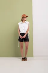 Camisa blanca sin mangas de lino y algodón, con cuello clásico, cierre frontal con botones, dos bolsillos con solapa en el pecho, hombreras y cordón ajustable en la cintura.