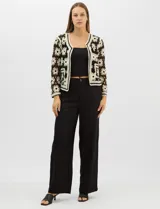 Cardigan abierto de tejido crochet con diseño de flores bicolores en negro y crema. Presenta mangas largas, frente abierto sin cierre y bolsillos frontales tipo parche. Posee terminaciones con franjas a contraste en escote, puños y ruedo.