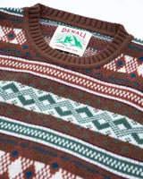 Buzo tejido de punto con diseño jacquard de motivos geométricos y nórdicos en tonos marrón, verde, blanco y azul. Presenta cuello redondo, puños y ruedo acanalados, y etiqueta de la marca Denali en el frente.