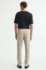 Pantalón de traje beige de corte slim fit, con cierre frontal con cremallera y corchete oculto, trabillas para cinturón, bolsillos laterales y bolsillos traseros ribeteados. Cuenta con raya marcada al frente.