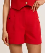 Short sastre de cintura alta, color blanco, con bolsillos laterales y detalles de tachuelas metalizadas.