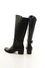 Bota de caña alta confeccionada en cuero legítimo color marrón, con diseño clásico, costuras visibles y una delicada tira con hebilla lateral. Cuenta con cierre lateral interno y taco medio ancho.
