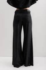Pantalón de pierna ancha con acabado brillante, confeccionado en lino. Presenta un diseño de tiro medio con cierre de botón y cremallera, bolsillos traseros y etiqueta de marca en la cintura.